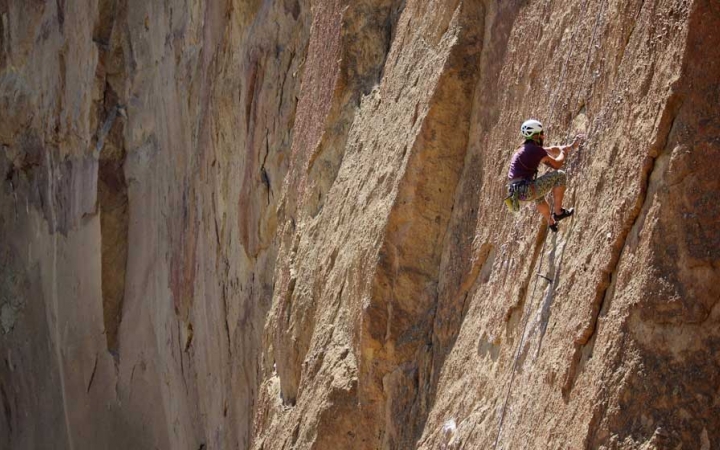 A person wearing safety gear is secured by ropes as they climb a tall rock wall. 